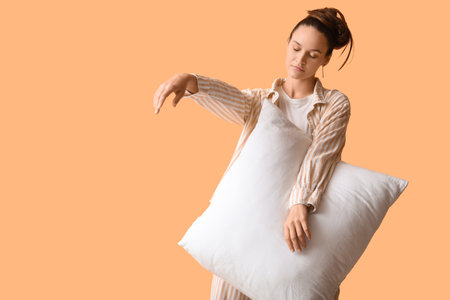 Female sleepwalker in pajamas with pillow on beige backgroundの写真素材