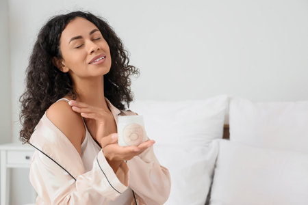 Young woman applying coconut oil to her shoulder in bedroomの写真素材