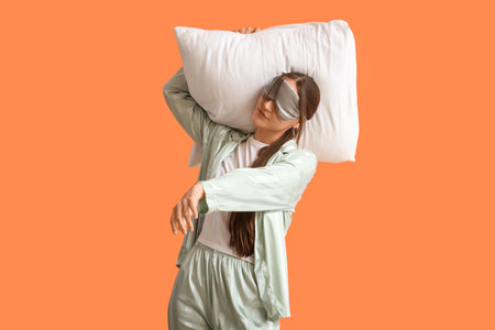 Female in pajamas with pillow on orange backgroundの写真素材