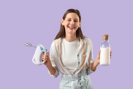Young woman with mixer and milk on lilac backgroundの写真素材