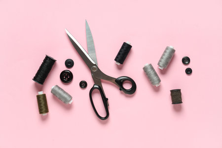 Thread spools with scissors and buttons on pink background