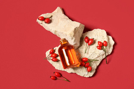Stones with bottle of cosmetic rose hip oil and berries on red backgroundの写真素材