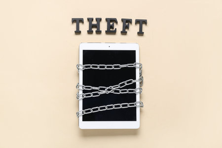 Tablet computer with chains and word THEFT on beige background