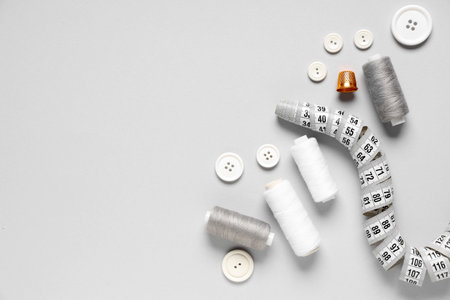 Thread spools with buttons, measuring tape and thimble on gray backgroundの写真素材