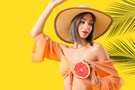 Beautiful young woman with grapefruit and palm leaves on yellow backgroundの写真素材