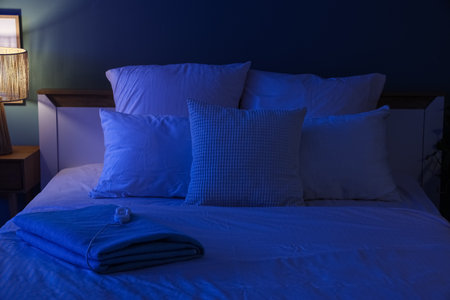 Folded electric heating pad on bed in dark roomの写真素材