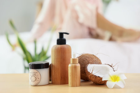 Cosmetic products with coconut oil and plumeria flower on table against woman in bedroom, closeupの写真素材