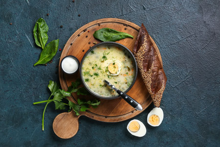 Bowl of tasty green borscht with eggs, sour cream, parsley, spinach leaves and baguette on blue grunge backgroundの写真素材