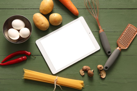 Digital recipe book with kitchen utensils and ingredients on green wooden backgroundの写真素材