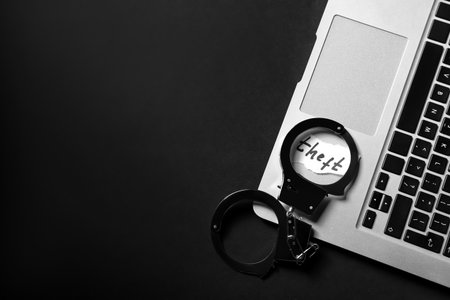 Paper with word THEFT, handcuffs and laptop on dark backgroundの写真素材
