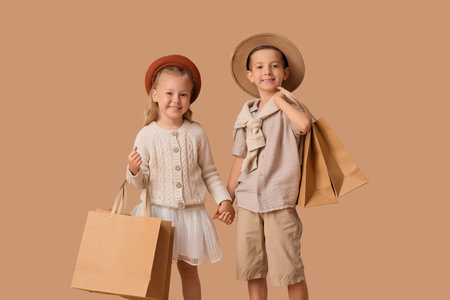 Stylish little children in hats with shopping bags on beige backgroundの写真素材