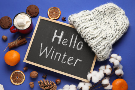 Chalkboard with text HELLO WINTER, hat, citruses and nuts on blue backgroundの写真素材