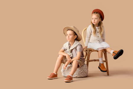 Stylish little children in hats sitting on beige backgroundの写真素材