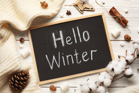 Chalkboard with text HELLO WINTER, marshmallows, cotton flowers and sweater on white wooden backgroundの写真素材