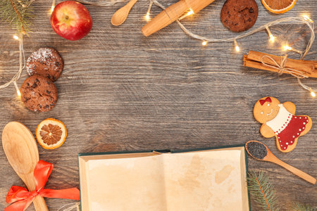 Frame made of recipe book with cookies, dried citruses and glowing Christmas lights on wooden backgroundの写真素材