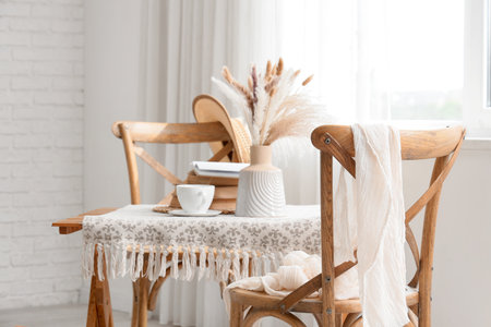 Interior of room with wooden chairs, vase, cup of tea and books on table near windowの写真素材