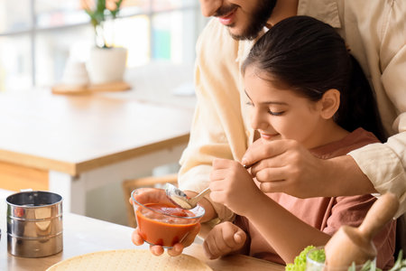 Father with his little daughter applying tomato sauce on pizza dough in kitchen, closeupの写真素材