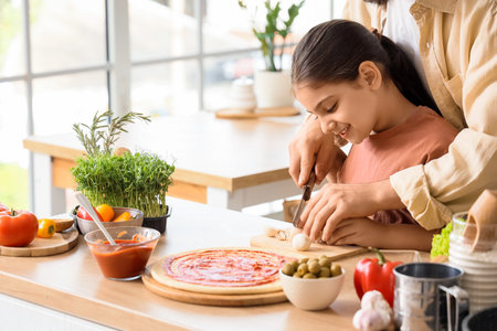 Father with his little daughter cutting mushrooms for pizza at table in kitchenの写真素材