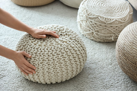 Female hands with knitted poufs on carpet in living room