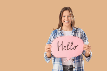 Young woman holding speech bubble with word HELLO on beige background