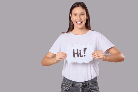 Young woman holding speech bubble with word HI on gray backgroundの写真素材