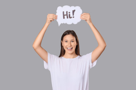 Young woman holding speech bubble with word HI on gray background