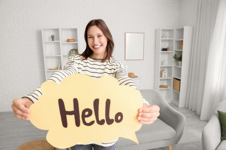 Young woman holding speech bubble with word HELLO at home