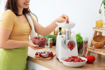 Young housewife using meat grinder in kitchen