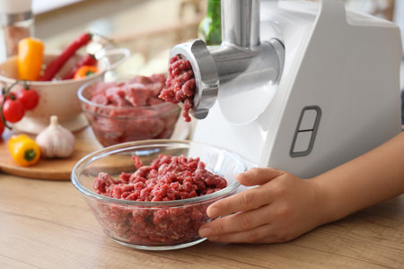 Hand using meat grinder on table in kitchen, closeup
