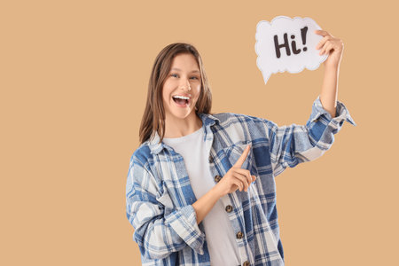 Young woman pointing at speech bubble with word HI on beige backgroundの写真素材