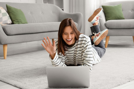 Happy young woman with laptop waving hand at home. Hello conceptの写真素材