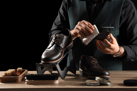 Male shoemaker polishing shoes at table on dark backgroundの写真素材