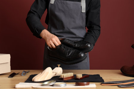 Male shoemaker with polished shoes at table on burgundy backgroundの写真素材