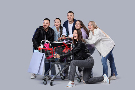 Group of young people with gifts in shopping cart on gray background. Cyber Mondayの写真素材