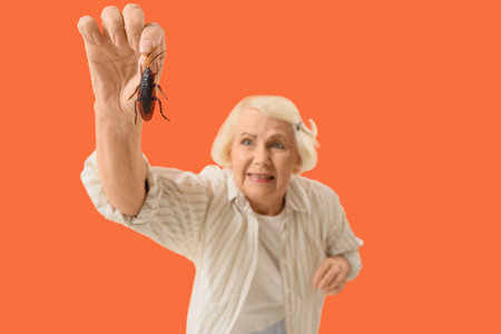 Senior woman with cockroach on orange background, closeupの写真素材