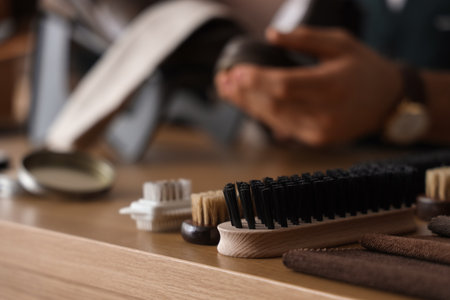 Cleaning brush on table against male shoemaker polishing boots in workshop, closeupの写真素材