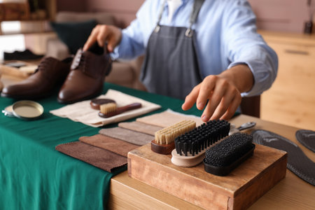 Male shoemaker with brushes polishing shoes in workshop, closeupの写真素材