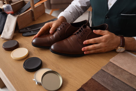 Male shoemaker with shoes and polishes at table in workshop, closeupの写真素材