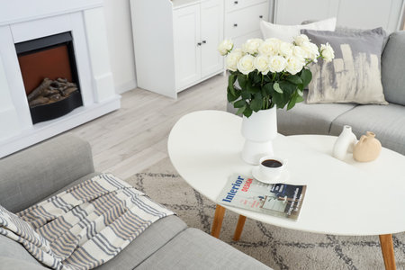 Vase with white roses, coffee cup and magazine on table in living roomの写真素材