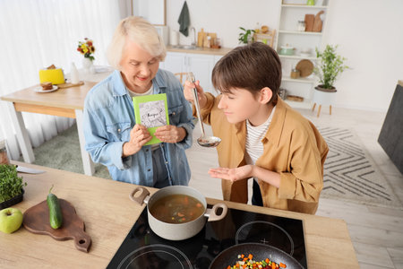 Senior woman with recipe book and her grandson tasting soup in kitchenの写真素材