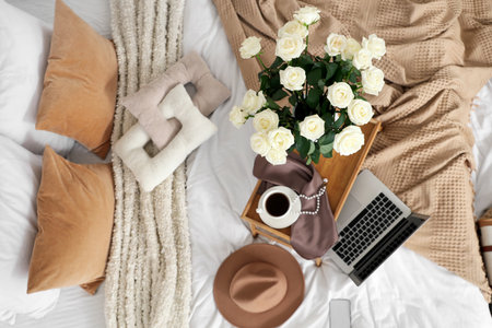Tray with white roses, coffee, laptop and accessories on bed, top viewの写真素材