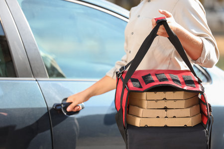 Male courier with pizza boxes in food bag near car on streetの写真素材