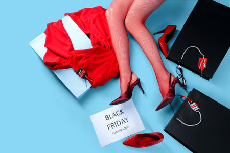 Young woman with shopping bags and new clothes lying on blue background, top view. Black Friday saleの写真素材