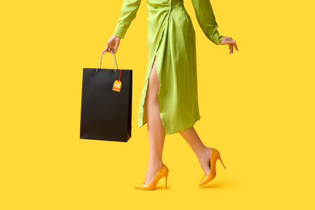 Beautiful young woman with shopping bag on yellow background, closeup. Black Friday saleの写真素材