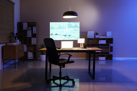 Interior of data scientist's office with workplace, shelving units, laptop and diagrams projection on wallの写真素材