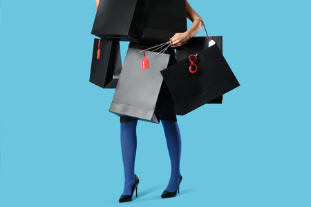 Beautiful young woman with many shopping bags on blue background, closeup. Black Friday saleの写真素材