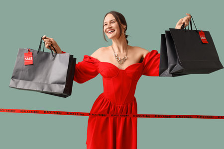 Happy young woman holding shopping bags and ribbon with text BLACK FRIDAY on turquoise backgroundの写真素材