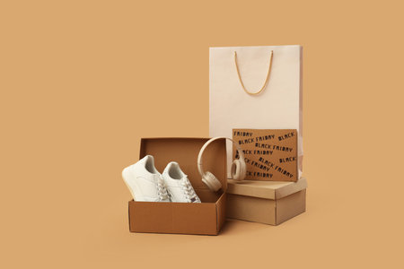 Shopping bag with boxes, sneakers and headphones on beige background. Black Friday sale concept
