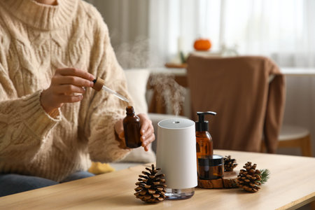 Woman adding essential oil to air humidifier on table in room, closeup