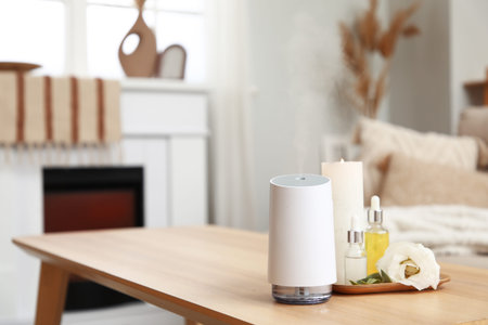 Air humidifier with essential oils, candle and eustoma flower on table in room